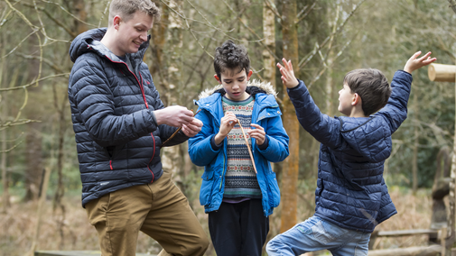 A parent and two children interacting within the woodland setting in winter